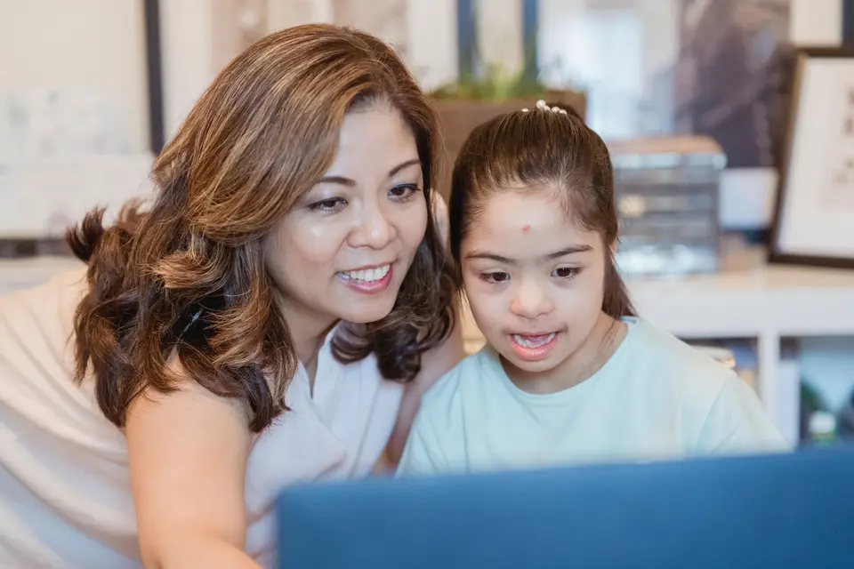 Een moeder en haar dochter met downsyndroom kijken lachend samen naar een laptop