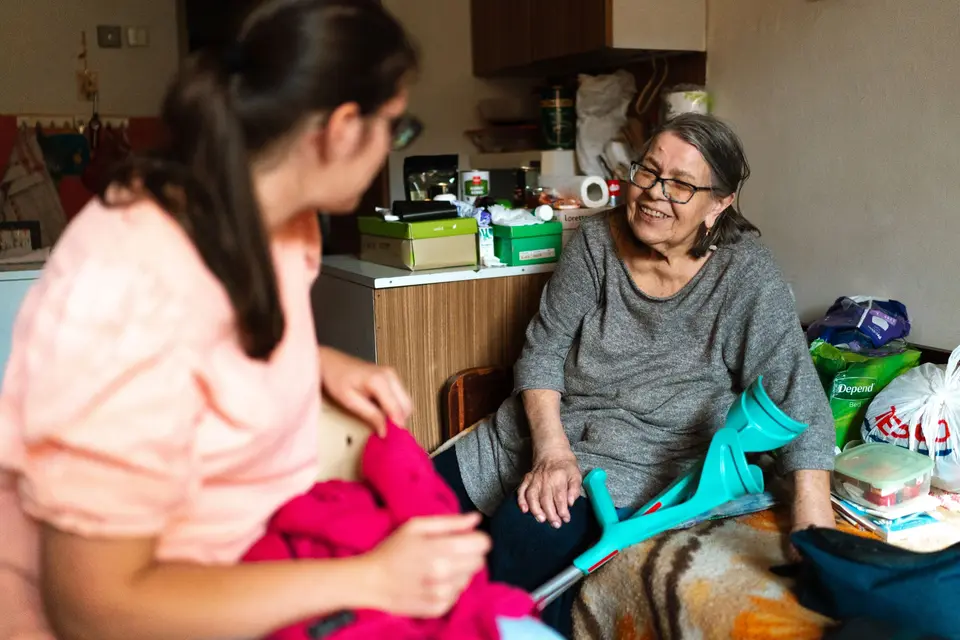 Een zorgverlener helpt een oudere vrouw met krukken bij haar thuis